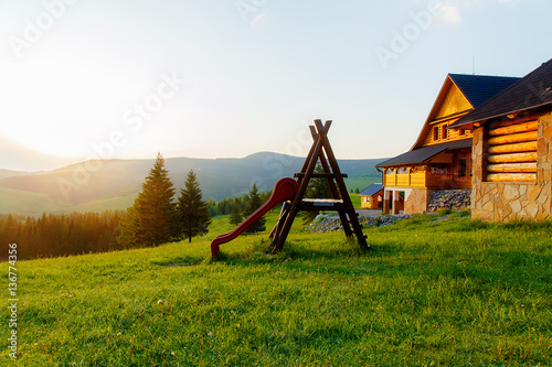 wooden children playground in highland landscape and small cottage..