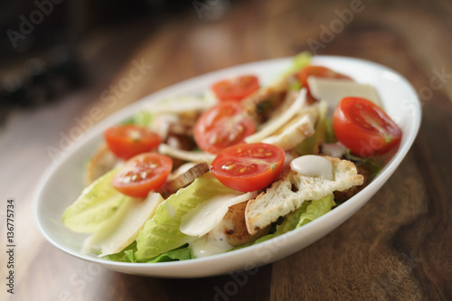 fresh caesar salad with chicken and cherry tomatoes on wood table, shallow depth of field