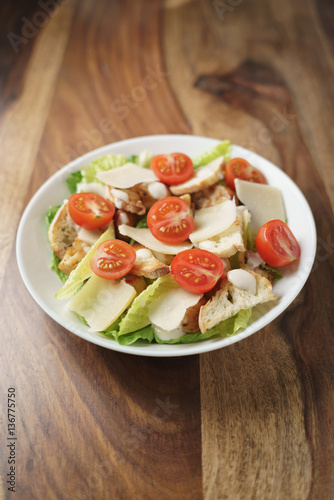 fresh caesar salad with chicken and cherry tomatoes on wood table, shallow depth of field