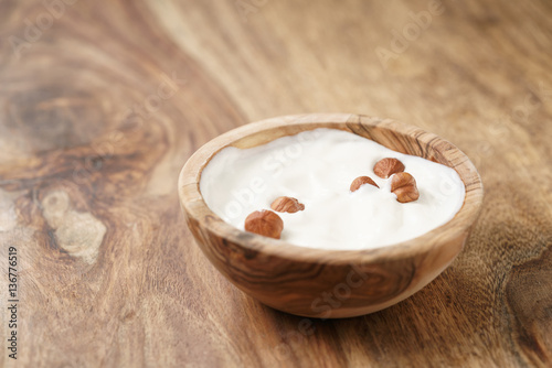 homemade yogurt with hazelnuts in wood bowl on wooden table, shallow focus