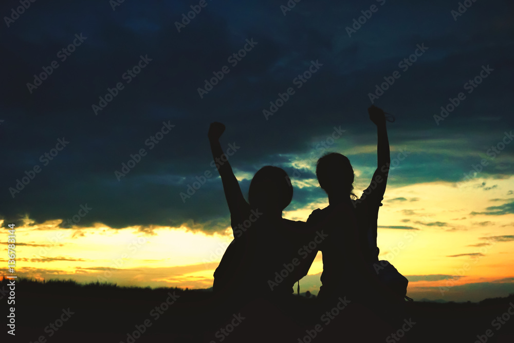 two female silhouettes sitting in front of a sunset sky with their arms raised two female silhouettes sitting in front of a sunset sky with their arms raised