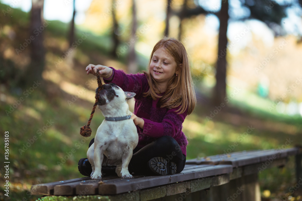Children and dogs outdoors. Beautiful and happy redhead girl enjoying and playing in autumn park with her adorable French bulldog. Children and dogs outdoors. Beautiful and happy redhead girl enjoying and playing in autumn park with her adorable French bulldog.