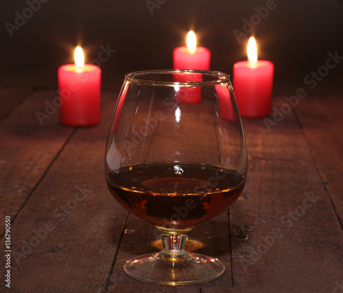 glass of wine or cognac and red candle on a wooden background. © v_l
