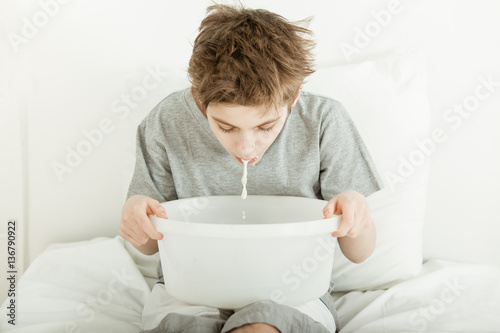 Young boy sitting in bed vomiting into a bowl