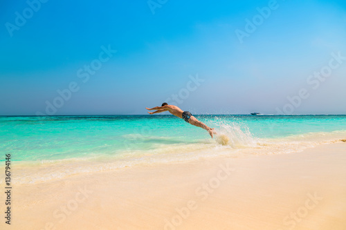 Happy young man jumping into the ocean