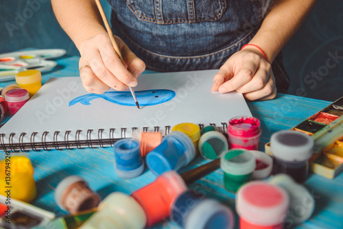 Pretty smiling young woman drawing a picture with poster paint