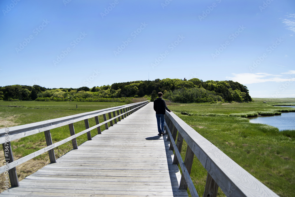 man walking along boardwalk over salt water marsh on Cape Cod