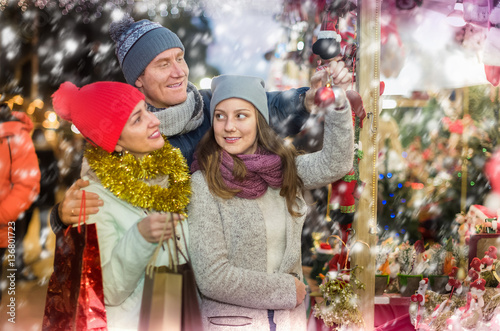 admiring family couple with teen daughter choosing Christmas dec
