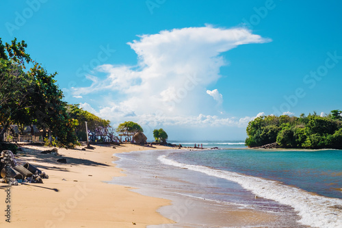 Beautiful outdooor landscape of white sand beach with tropical palm trees in Nusa Dua, Bali island, Indonesia. Blue sky with fantastic white clouds at a sea shore with tropical island exotic nature photo