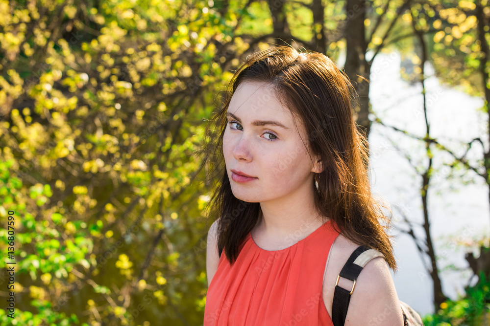Pretty young girl in a red dress with a backpack in the park on a sunny day Pretty young girl in a red dress with a backpack in the park on a sunny day