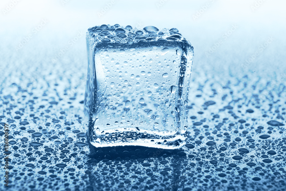 Transparent ice cube with reflection on blue glass with water drops Transparent ice cube with reflection on blue glass with water drops