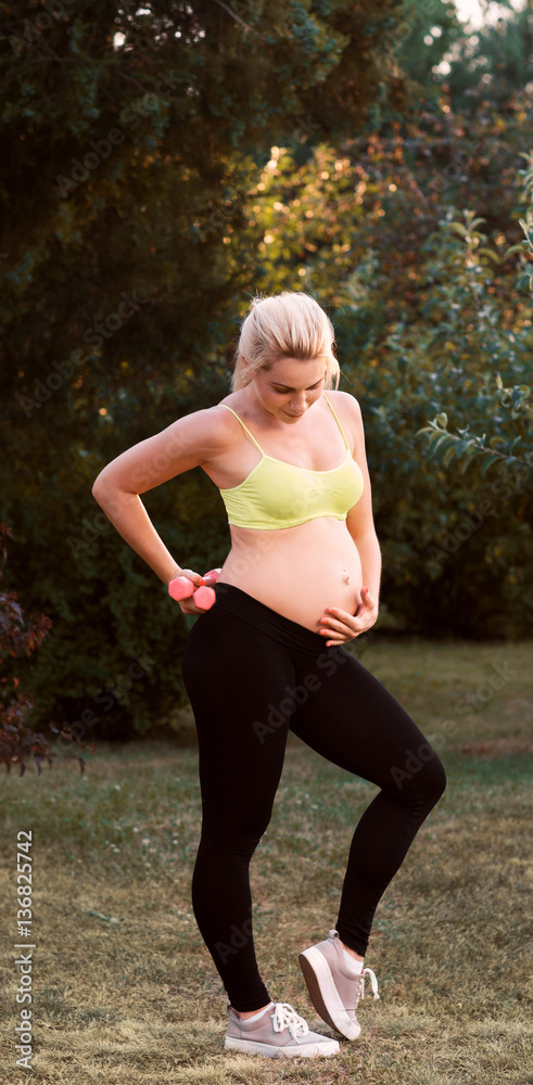 Fitness pregnant woman feeling her baby push. Happy gravid blonde touching  her belly while doing fitness exercises at nature. Pregnancy sport at  nature, healthy lifestyle, body care concept Stock Photo | Adobe