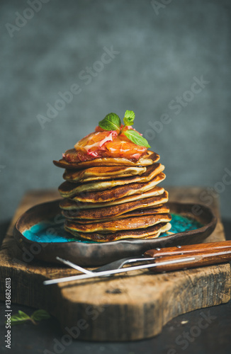 Homemade pancakes with honey, bloody orange slices and mint leaves for breakfast on blue ceramic plate over rustic wooden board, grey plywood wall at background, selective focus, copy space