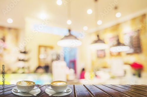 Two coffee cups on brown wooden table over blurred photo of beautiful coffee shop for background use
