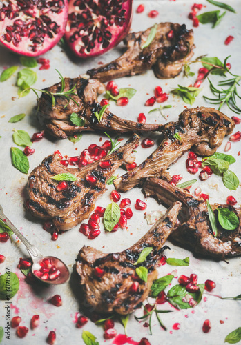 Grilled lamb ribs with pomegranate seeds, fresh mint and rosemary in metal baking tray. Meat barbecue and slow food concept. Selective focus