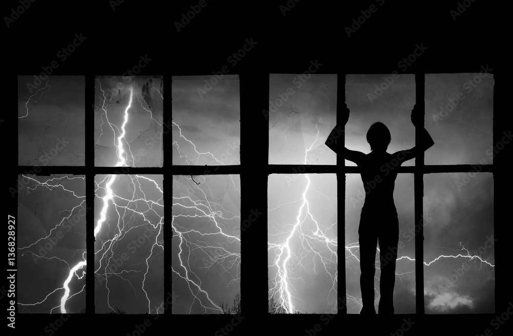 Fototapeta premium Silhouette of man watching lightning, thunder, rain and storm through the broken window of abandoned building