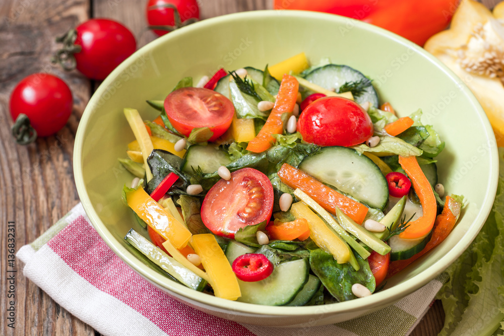 Fresh salad with vegetables, greens and pine nuts on wooden background