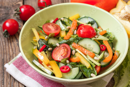 Fresh salad with vegetables, greens and pine nuts on wooden background