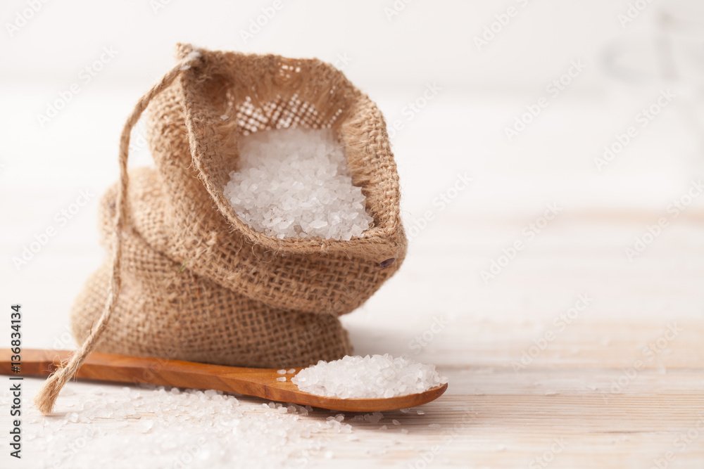 sea salt in the bag and wooden spoon on white wooden background
