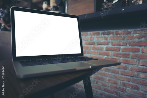 Mockup image of laptop with blank white screen on wooden table with red bricks wall background in dark modern cafe