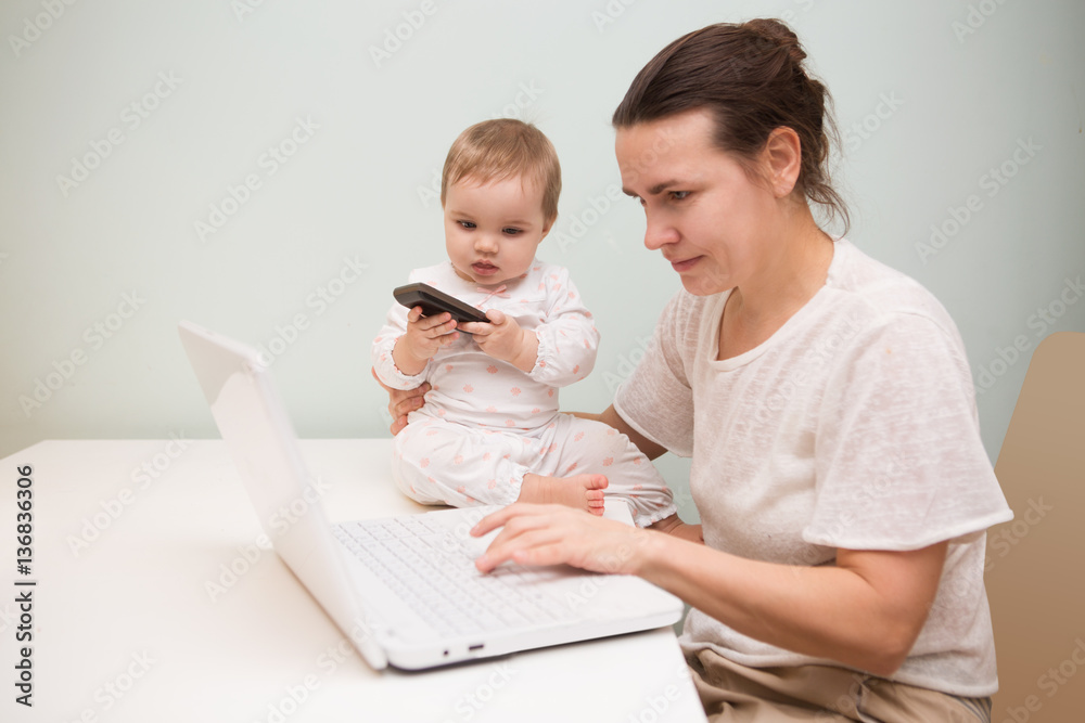 mom and baby. a young mother working with laptop in kitchen mom and baby. a young mother working with laptop in kitchen