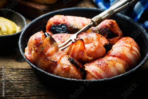Sausages with prunes and bacon in iron pan