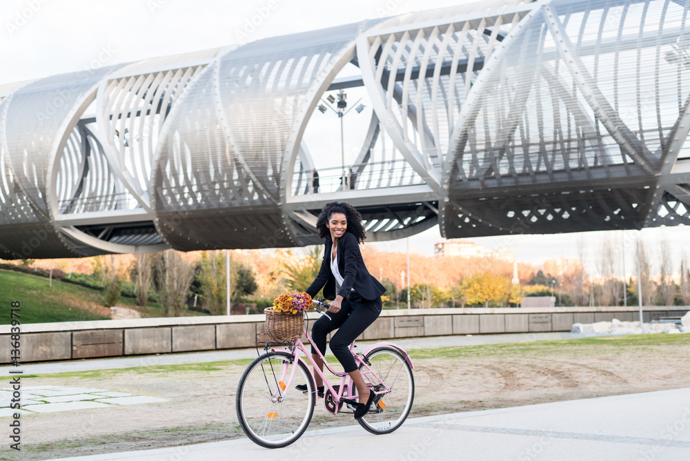 Fototapeta premium Business black woman riding a vintage bicycle in the city