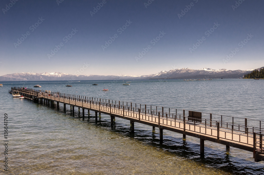Boats and pier in Lake Tahoe with snowy mountains background
