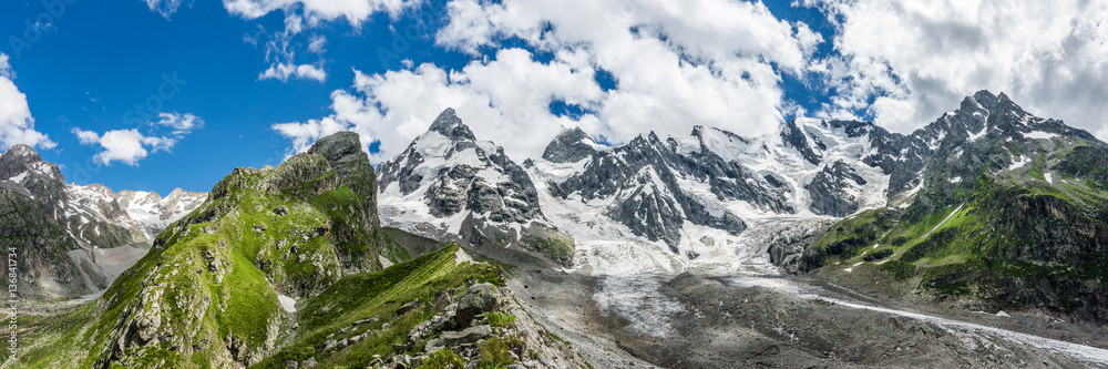 Summer panorama view of the Caucasian snow coverd peaks and the glacier at the foot of it. Russia, Kabardino-Balkaria, Elbrus region.