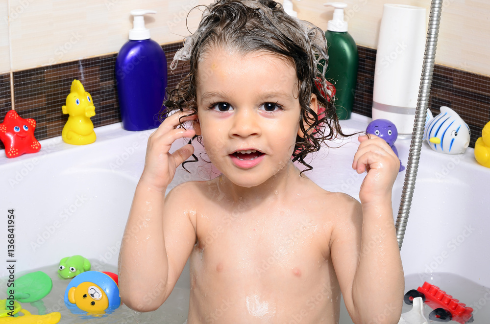 Beautiful toddler taking a bath in a bathtub with bubbles. Cute kid washing his hair with