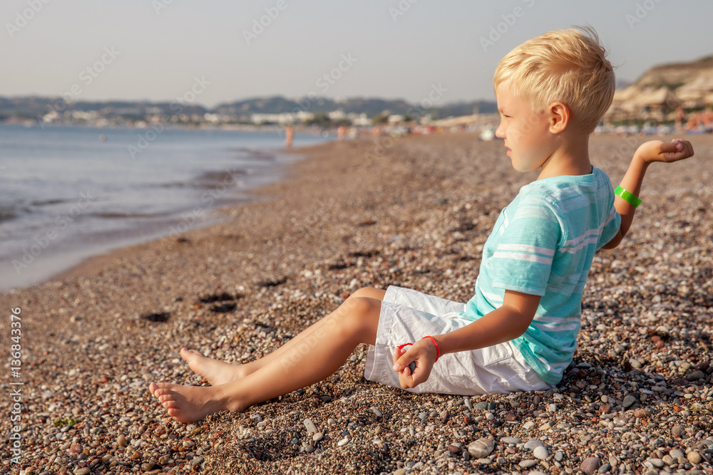 Happy smiling small boy sitting on the beach and playing with stones. Happy smiling small boy sitting on the beach and playing with stones.