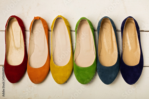 Row of colorful shoes (ballerinas) on a white wooden background.