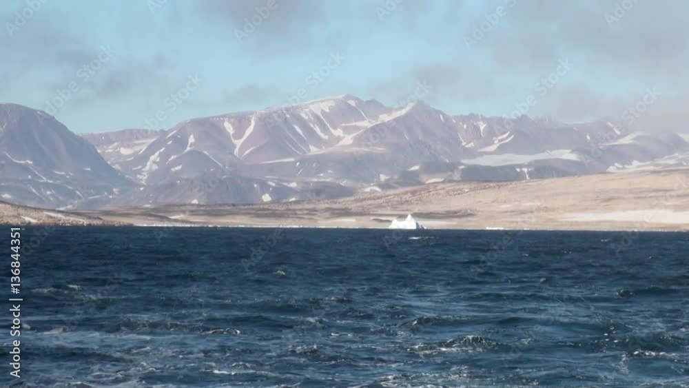 Snowy mountains in background waves on shore of Greenland in Arctic Ocean. Wilderness. Extreme tourism and travel in the cold polar north. Scenic coastline and blue water. Iceland. Snowy mountains in background waves on shore of Greenland in Arctic Ocean. Wilderness. Extreme tourism and travel in the cold polar north. Scenic coastline and blue water. Iceland.