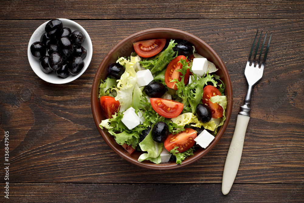 Fresh greek salad in bowl on the wooden table.