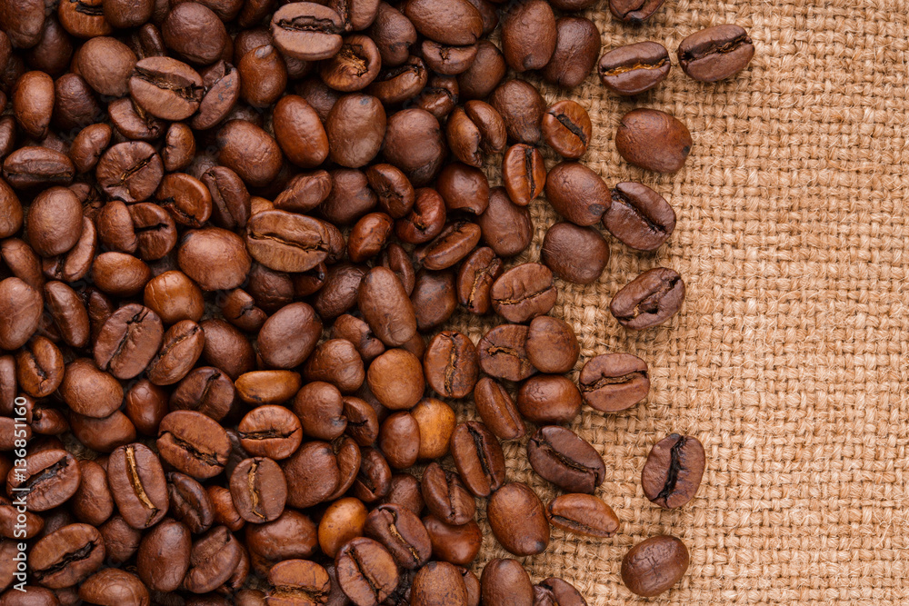 Fototapeta premium coffee beans on burlap background. roasted coffee beans isolated in white background. Roasted coffee beans background close up. Coffee beans pile from top on white background with copy space for text