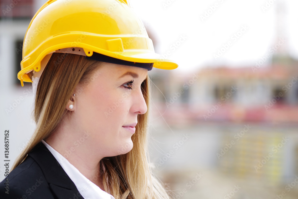 Junge Frau mit Helm und Plänen vor einer Baustelle Junge Frau mit Helm und Plänen vor einer Baustelle