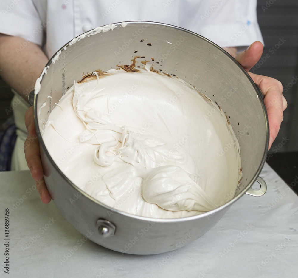 A beautiful rich and creamy , white whipped meringue mixture in a large metal mixing bowl. A beautiful rich and creamy , white whipped meringue mixture in a large metal mixing bowl.