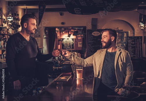 Stylish man paying for beer by card to bartender in pub.