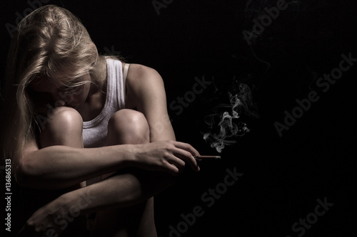sad smoking blond girl on black background