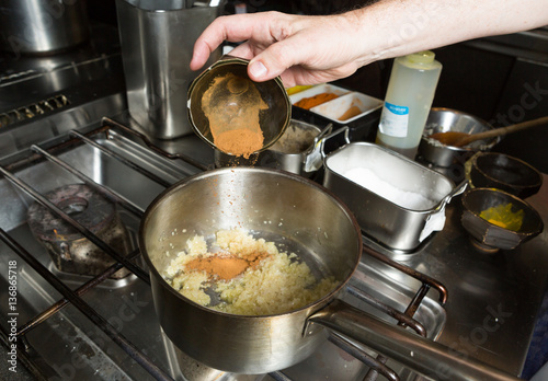 Turmeric powder being dropped into a pan of frying  minced garlic and finely sliced onion. Step by step recipe cooking.
