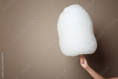 Female hand holding cotton candy on color background