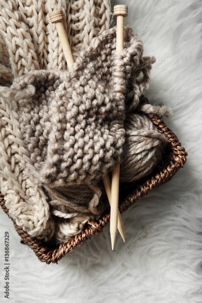 Fototapeta premium Knitting yarn and needles in wicker basket on white fluffy carpet