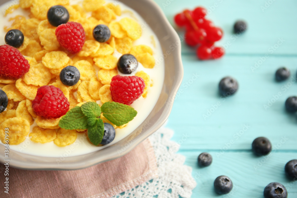 Tasty cornflakes with raspberries and blueberries on blue background