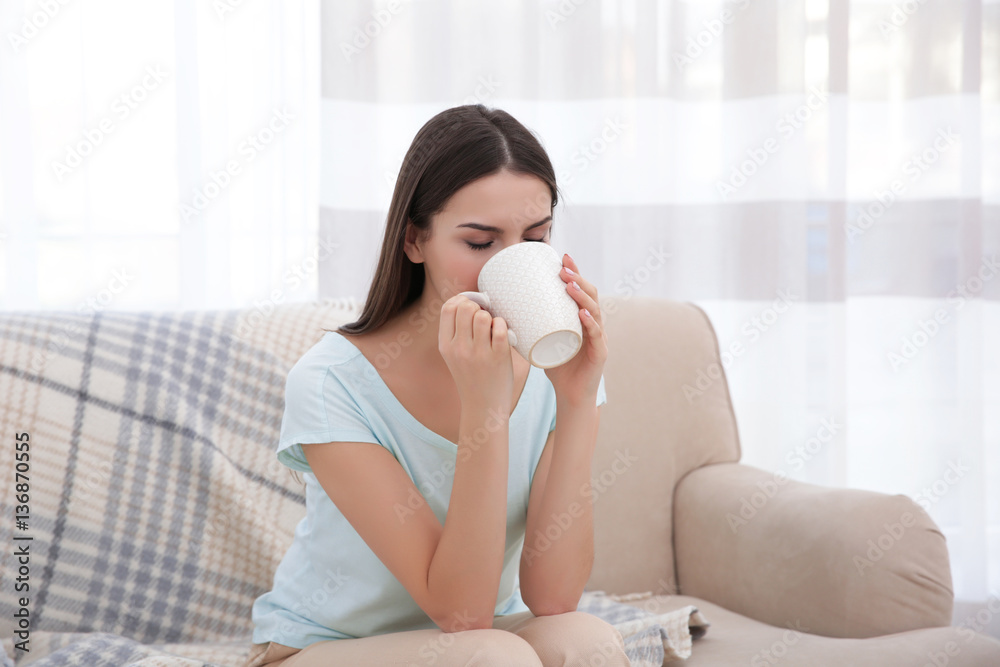 Young woman resting on couch and drinking tea in light room Young woman resting on couch and drinking tea in light room