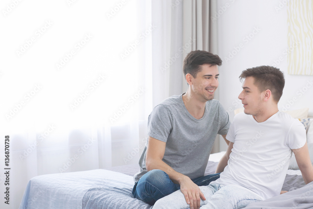 Happy gay couple sitting on bed at home