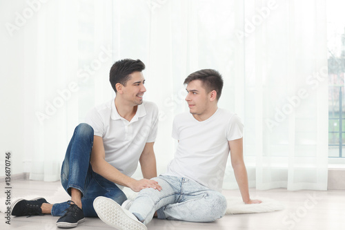 Happy gay couple sitting on floor against window