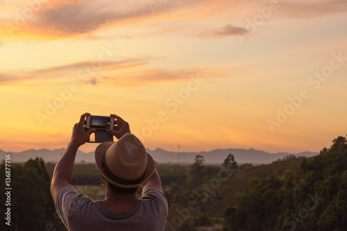 Male hipster taking photo with smartphone in his hand with sunset view.Dark tone © engkritchaya