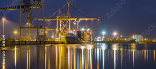 unloading cargo ship with containers in sea port at night