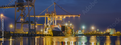 unloading cargo ship with containers in sea port at night