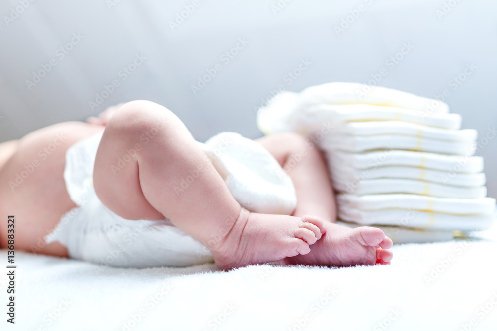 Feet of newborn baby on changing table with diapers - obrazy, fototapety, plakaty 